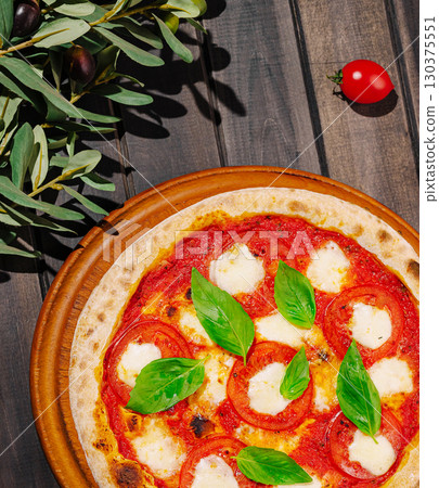Freshly made pizza with tomatoes and basil on a rustic wooden table 130375551