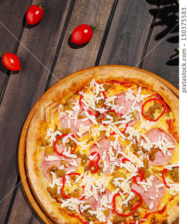 Delicious pizza topped with ham, cheese, and chili peppers in a sunny setting 130375583