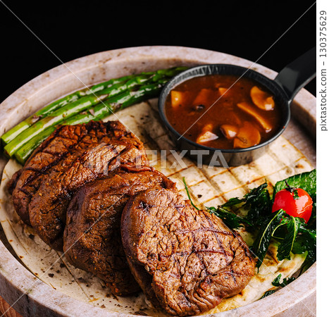 Grilled steak served with vegetables and sauce on a wooden board 130375629
