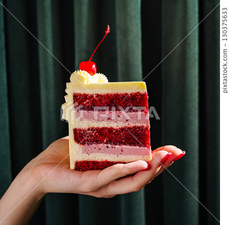 Delicious multicolored cake served with a cherry on top held in a hand Delicious multicolored cake served with a cherry on top held in a hand 130375633