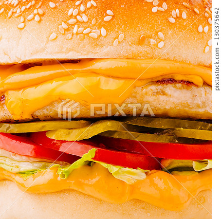 Delicious burger with cheese, lettuce, tomatoes, and pickles on a sesame bun 130375642