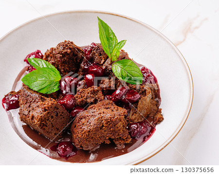 Chocolate dessert with cherry sauce and mint garnish placed in a white bowl 130375656