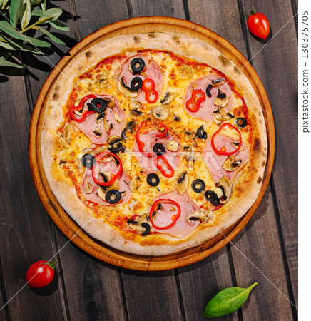 Delicious pizza with ham, olives, and vegetables on a rustic wooden table 130375705