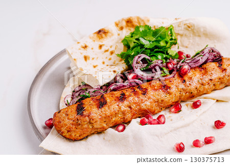 Grilled kebab served with fresh herbs, onions, and pomegranate seeds Grilled kebab served with fresh herbs, onions, and pomegranate seeds 130375713