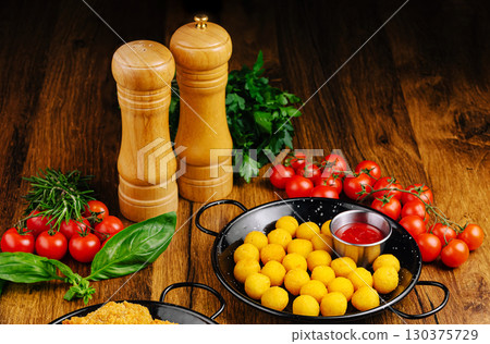 Delicious snack platter with golden balls, tomatoes, and herbs on rustic table 130375729