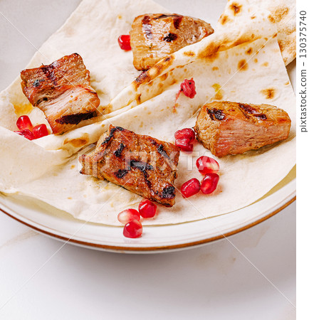 Grilled meat served on flatbread with pomegranate seeds in elegant presentation Grilled meat served on flatbread with pomegranate seeds in elegant presentation 130375740
