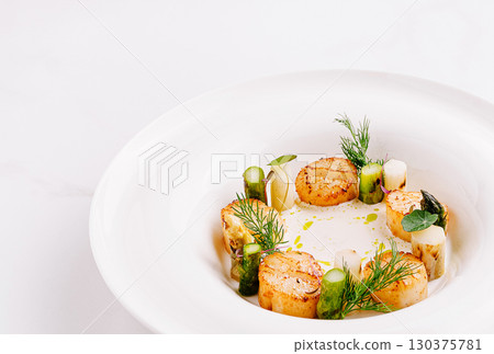 Seared scallops served on a delicate puree with fresh herbs and vegetables 130375781