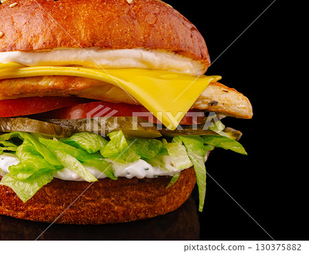Tasty cheeseburger with chicken, lettuce, and veggies on black Tasty cheeseburger with chicken, lettuce, and veggies on black 130375882