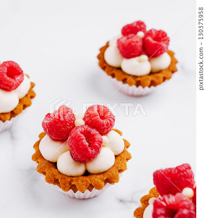 Mini raspberry tarts with cream on a white marble surface 130375958
