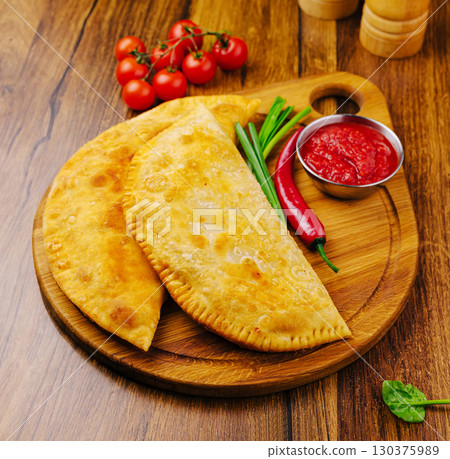 Fried pastries with fresh veggies and sauce on a wooden board 130375989