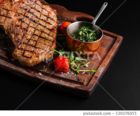 Grilled steak served with fresh herbs and tomatoes on wooden board Grilled steak served with fresh herbs and tomatoes on wooden board 130376055