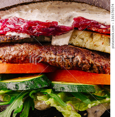 Gourmet burger with fresh vegetables and savory sauce in a dark bun Gourmet burger with fresh vegetables and savory sauce in a dark bun 130376074
