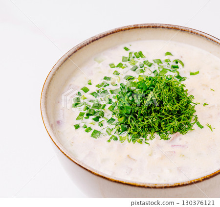 Creamy soup topped with green herbs in a bowl on a light surface 130376121