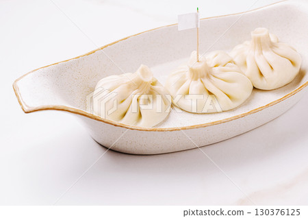 Dumplings or khinkali served elegantly on a white dish at a culinary event Dumplings or khinkali served elegantly on a white dish at a culinary event 130376125
