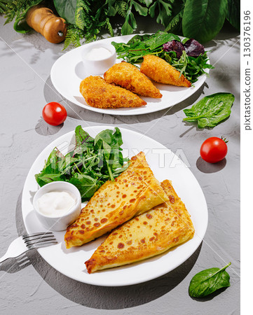 Savory dishes featuring stuffed pastries and fresh salad on a bright table Savory dishes featuring stuffed pastries and fresh salad on a bright table 130376196