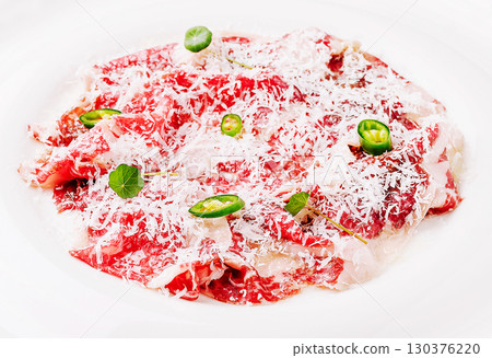 Premium raw beef carpaccio with garnishes and grated cheese on a plate 130376220
