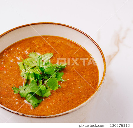 Delicious bowl of soup garnished with fresh cilantro on a white background 130376313