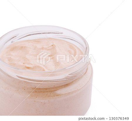 Glass jar filled with creamy light beige sauce or dip, smooth texture, isolated on white background 130376349