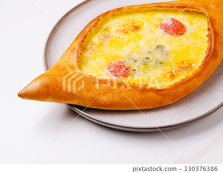 Delicious adjarian khachapuri served on a round plate in a bright setting 130376386