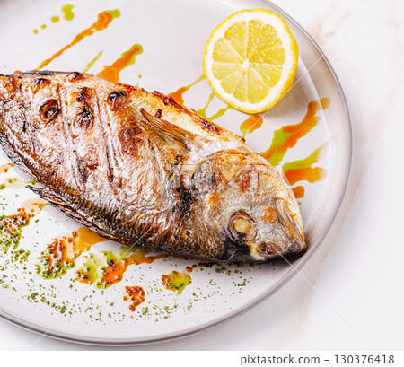Grilled fish served with lemon on a white plate at a restaurant 130376418