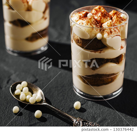 Delicious tiramisu dessert layered with creamy filling and sponge cake in elegant glass 130376442