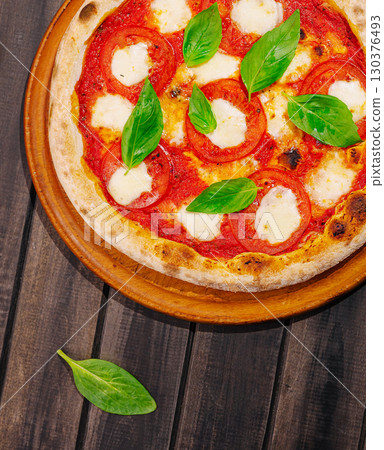 Freshly baked pizza with tomatoes and basil on a wooden table Freshly baked pizza with tomatoes and basil on a wooden table 130376493