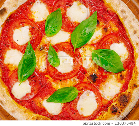 Freshly baked Margherita pizza topped with basil and tomatoes 130376494