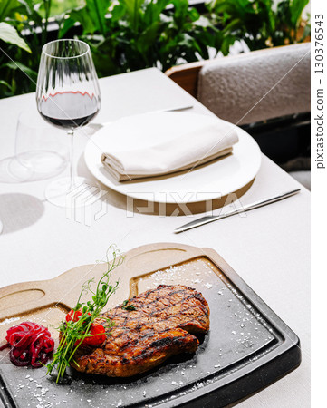 Delicious grilled steak served with wine on a dining table near greenery Delicious grilled steak served with wine on a dining table near greenery 130376543