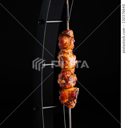 Juicy grilled meat skewers hanging on a metal stand at a barbecue event 130376648