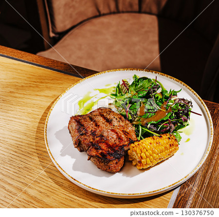 Grilled steak served with salad and corn on a wooden table Grilled steak served with salad and corn on a wooden table 130376750