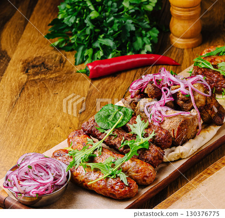 Grilled meat platter with fresh herbs and toppings served on a wooden board Grilled meat platter with fresh herbs and toppings served on a wooden board 130376775