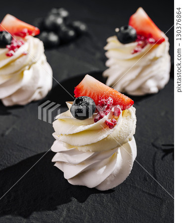 Delicious meringue desserts topped with fresh fruits on dark background Delicious meringue desserts topped with fresh fruits on dark background 130376864