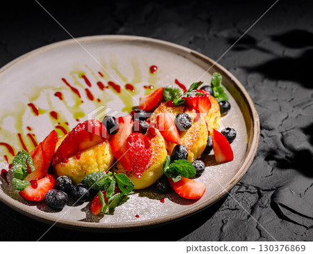 Dessert plated with berries and mint garnishes on a dark textured surface 130376869