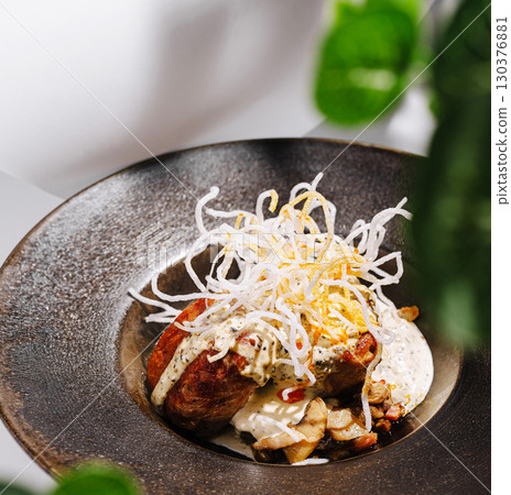 Gourmet plate featuring meat, sauce, and crispy toppings in modern setting 130376881