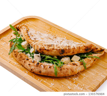 Delicious flatbread filled with fresh greens and cheese on a wooden platter Delicious flatbread filled with fresh greens and cheese on a wooden platter 130376984