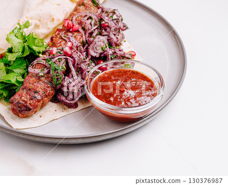 Delicious kebab served with fresh salad and spicy sauce on a plate Delicious kebab served with fresh salad and spicy sauce on a plate 130376987