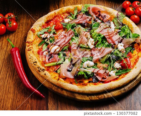 Delicious pizza topped with greens, ham, and cheese served on wooden board Delicious pizza topped with greens, ham, and cheese served on wooden board 130377082