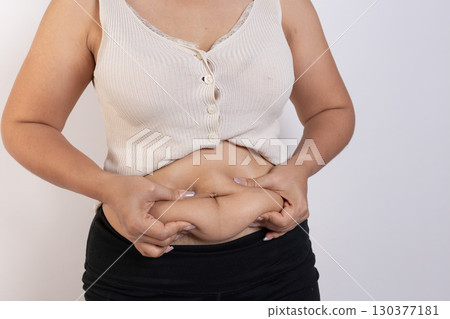 Overweight woman hand pinching excessive belly fat on gray background, Healthy concept 130377181