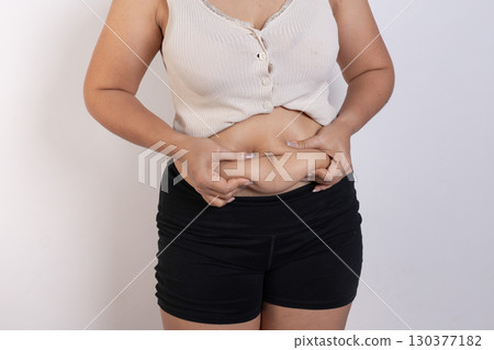 Overweight woman hand pinching excessive belly fat on gray background, Healthy concept Overweight woman hand pinching excessive belly fat on gray background, Healthy concept 130377182