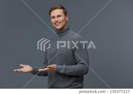 smiling caucasian man in gray sweater present gesture digital nomad casual wear isolated gray background studio portrait smiling caucasian man in gray sweater present gesture digital nomad casual wear isolated gray background studio portrait 130377227