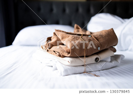 Neatly folded brown and beige clothes on white bed in calm bedroom atmosphere 130379845