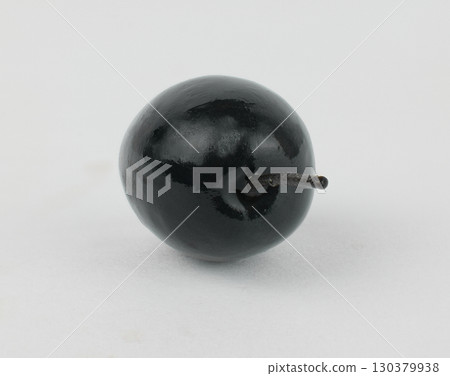Single black olive resting on a plain surface Single black olive resting on a plain surface 130379938