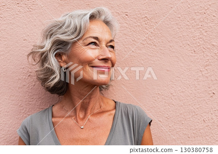 Middle-aged woman with healthy hair smiling against a pink wall at an urban location 130380758