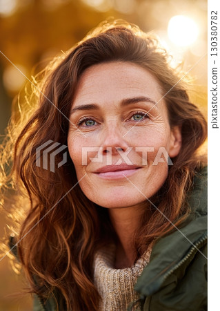 Woman with clear skin and bright eyes enjoying autumn sunlight in a serene outdoor setting 130380782