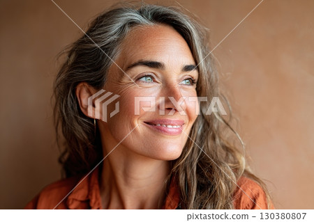 Woman with long hair smiles gently, showcasing joy and confidence in a warm setting 130380807