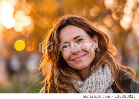 Middle-aged woman smiles warmly during autumn evening stroll in a park 130380823