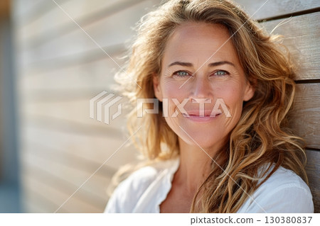 Middle-aged woman with long wavy hair smiling against a wooden backdrop in natural light Middle-aged woman with long wavy hair smiling against a wooden backdrop in natural light 130380837