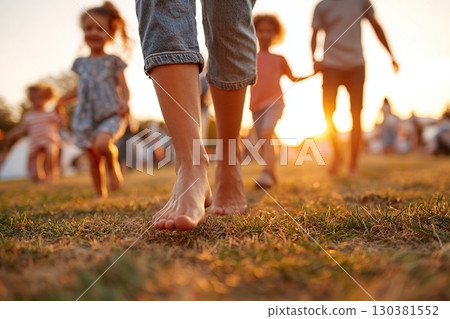 Walking barefoot on grass in a sunny park with children during evening hours 130381552