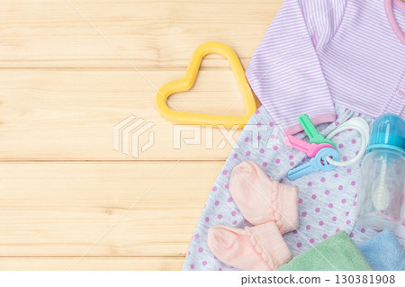 Infant wear and baby rattle with feeding bottle. Kid's care concept, copy space for text. Baby pink bodysuit for newborn girl and toys on wooden background with copy space for text Infant wear and baby rattle with feeding bottle. Kid's care concept, copy space for text. Baby pink bodysuit for newborn girl and toys on wooden background with copy space for text 130381908