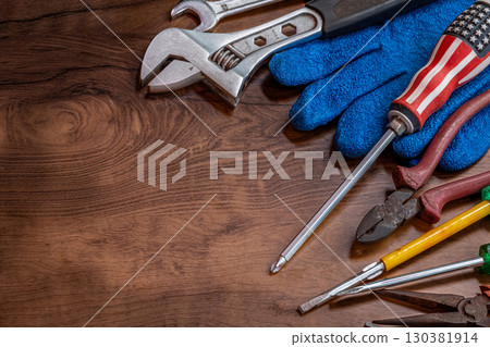 Different working tools on dark wooden background. Hand tools and the Flag of the United States of America lying on the table. View from above, close-up. National USA holiday celebration concept Different working tools on dark wooden background. Hand tools and the Flag of the United States of America lying on the table. View from above, close-up. National USA holiday celebration concept 130381914